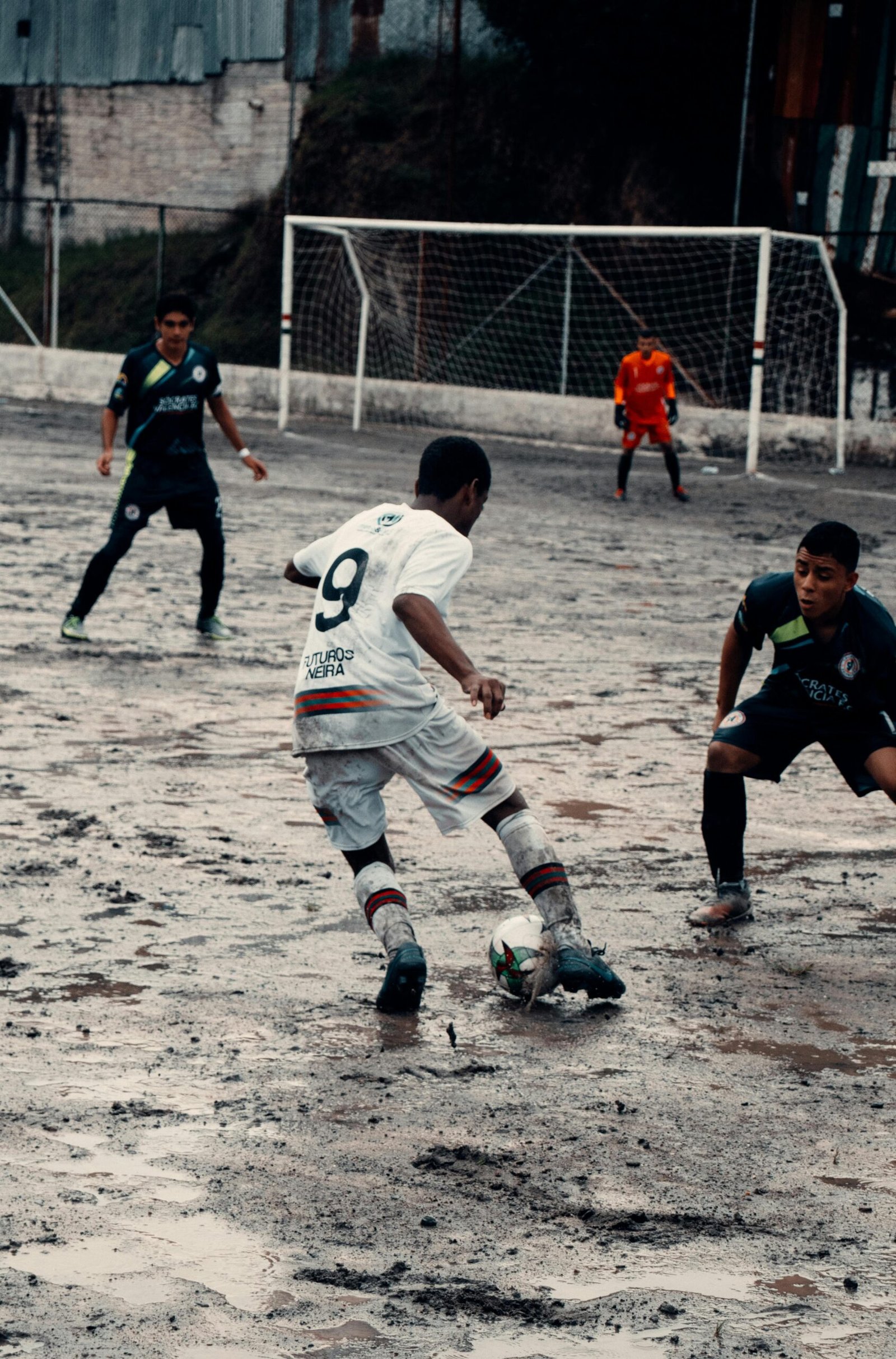 Young soccer players compete intensely on a muddy field in Neira, Colombia.