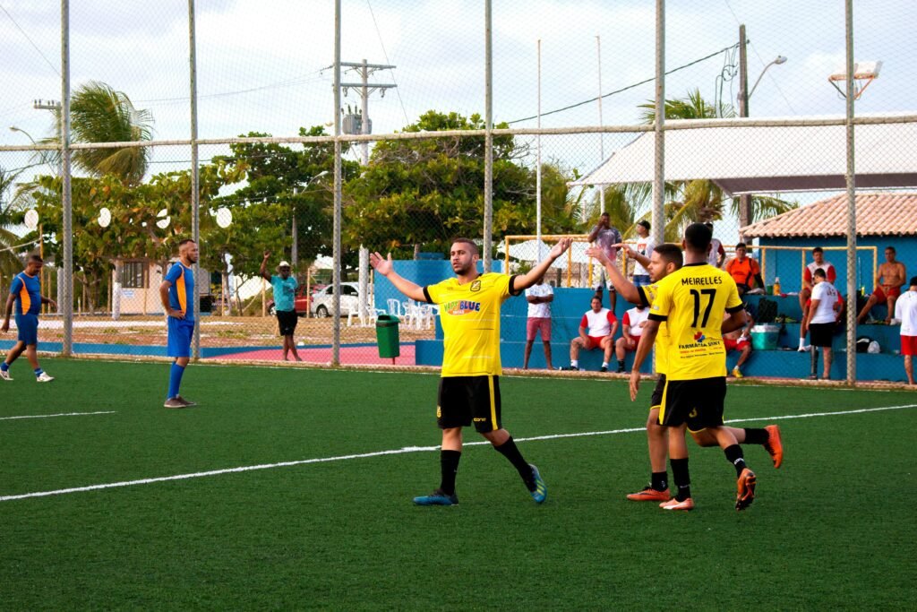 Amateur soccer team in yellow jerseys celebrates a goal during a match on an outdoor field.